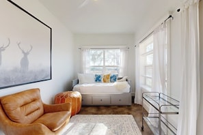 A bedroom with a bed, a chair, a bedside table, a window, and a framed picture on the wall.