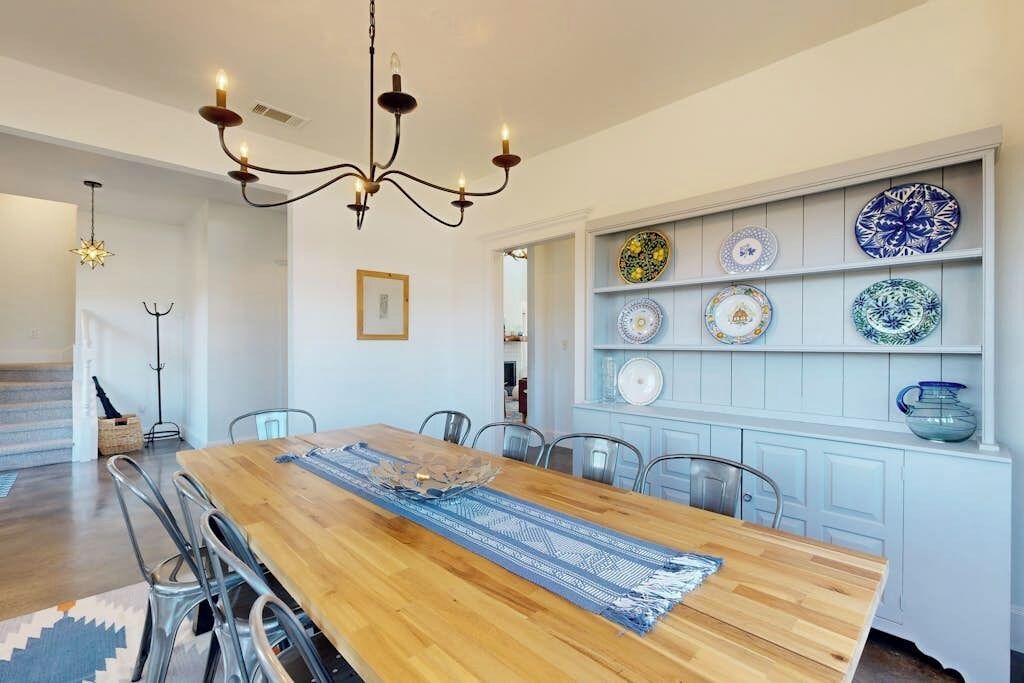 Een eethoek met een houten tafel, stoelen, een kroonluchter en een wandplank met borden.