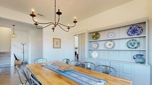 Un comedor con mesa de madera, sillas, candelabro y una exposición de platos en la pared.
