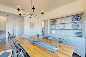 A dining area with a wooden table, chairs, a chandelier, and a wall-mounted plate display.