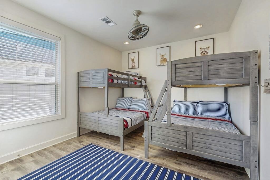 Een kamer met twee stapelbedden, een plafondventilator en een raam met jaloezieën.