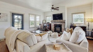 A spacious living room with a fireplace, a sofa, a coffee table, and a television. - Cozy ranch home w/full kitchen, living room, hot tub, pet-friendly & fireplace (Fredericksburg)