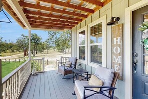 Eine überdachte Veranda mit Holzboden, eine Sitzecke mit Sofa und Sesseln, große Fenster und ein Schild mit der Aufschrift 'HOME' an der Tür.