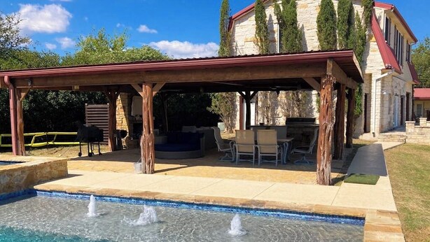 A pool with a wooden deck and a covered seating area. - Spicewood Lake Retreat | Pool + Shuffleboard (Spicewood)