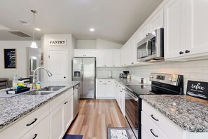 Eine moderne Küche mit weißen Schränken, Granit-Arbeitsplatten, Edelstahlgeräten und einem sichtbaren Vorratsschrankbereich.