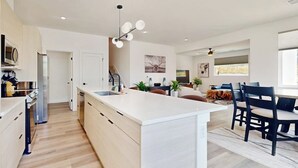 Une cuisine moderne dotée d’un îlot central, un coin repas avec une table et des chaises, et un espace de vie comprenant un canapé et un téléviseur.