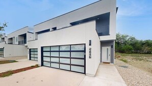 Une maison moderne à deux étages, dotée d’un garage, d’un toit plat et d’un petit balcon.