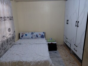 Ein Schlafzimmer mit Bett, Nachttisch, Kleiderschrank und einem gemusterten Vorhang.