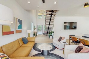 Uma sala de estar moderna com escada, área de refeições e TV fixada na parede.