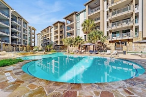 A multi-story hotel with a swimming pool, outdoor seating, and palm trees.