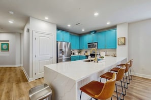 A modern kitchen with a large island, blue cabinets, stainless steel appliances, and a bar stool seating area.