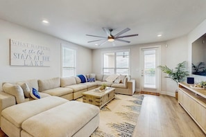 A living room with a sectional sofa, a coffee table, a ceiling fan, and a wall-mounted TV.