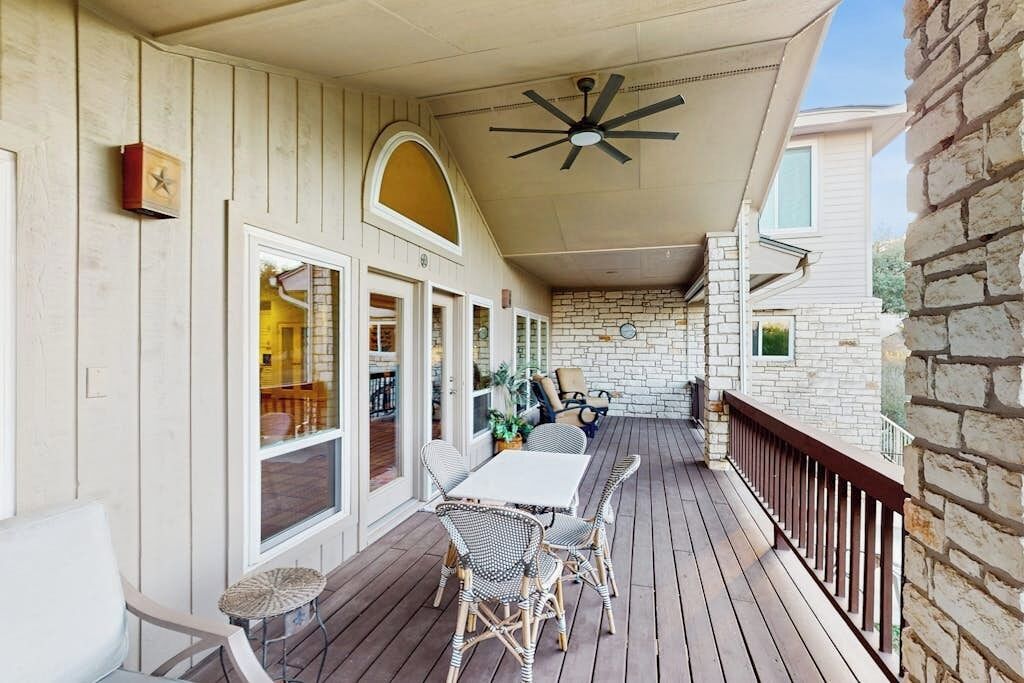 A covered outdoor patio with a table and chairs, a ceiling fan, and a stone wall.