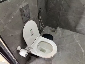 Un baño con inodoro blanco, ducha y suelo de mármol.