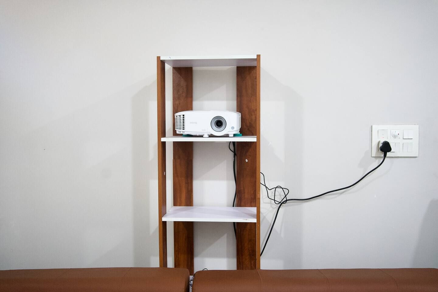 A projector on a shelf with a power cord plugged into a wall socket.