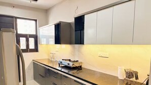 A modern kitchen with a refrigerator, stove, and cabinets. - Amur Stays 4: 6 Bedroom Independent Floors (Sahibzada Ajit Singh Nagar)