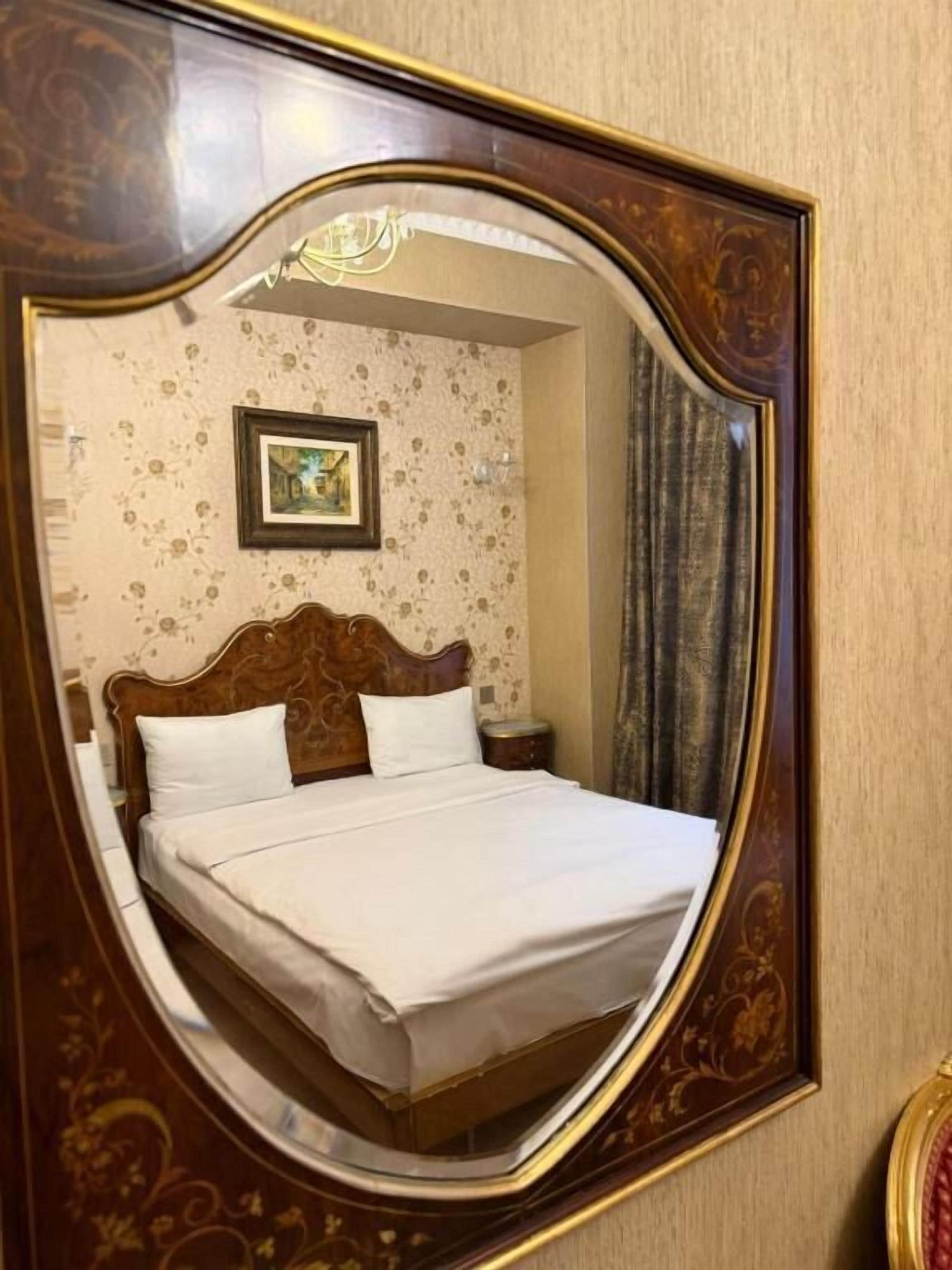 A room with a bed, a nightstand, a framed picture on the wall, and a mirror with an ornate frame.
