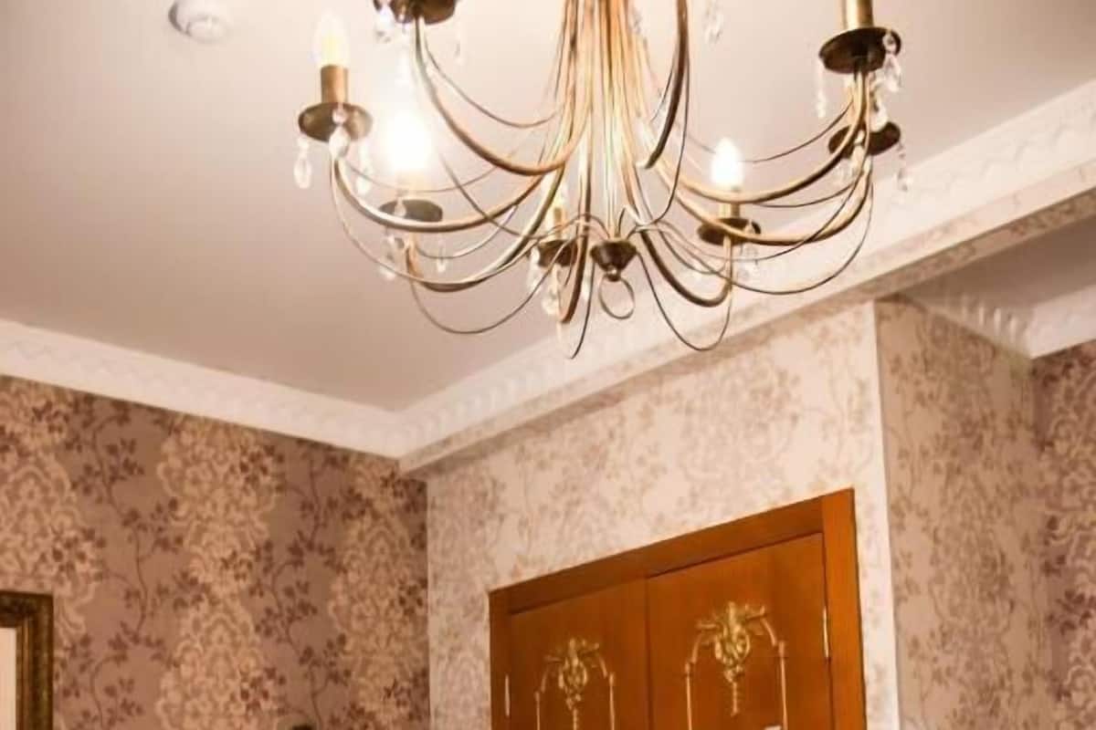 A bedroom with a bed, a wooden wardrobe, a mirror, and a chandelier.