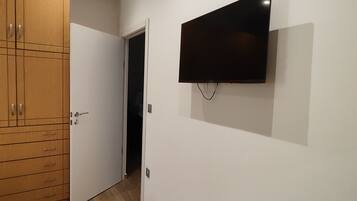 Ein Zimmer mit einem Holzkleiderschrank, einem an der Wand montierten Fernseher und einem gelben Bett.
