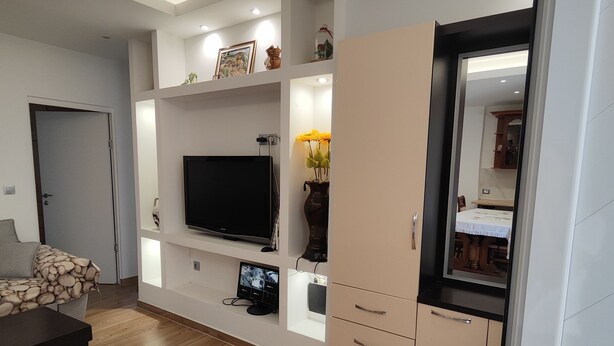 Una sala de estar moderna con una televisión de pantalla plana, piso de madera, un sofá y un mueble con cajones.