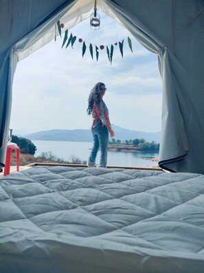 Une tente avec un lit, une vue sur un lac et un tabouret rouge.