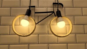 Una lámpara de pared con dos bombillas, unidas por una estructura de metal negro.