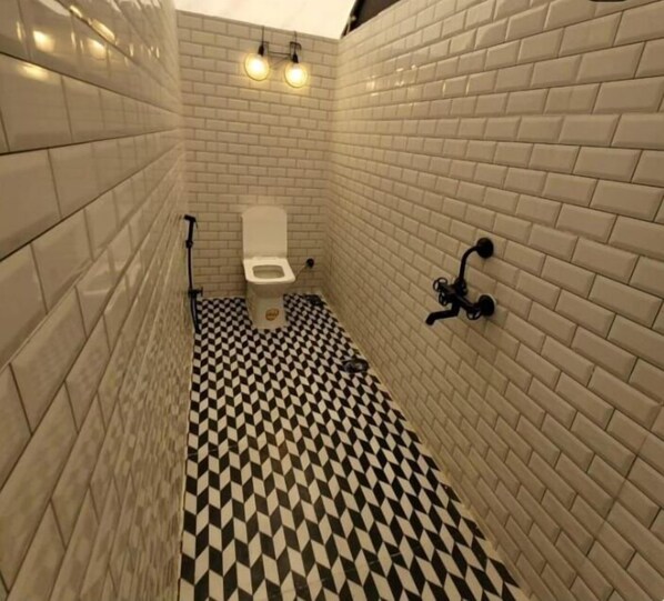 A bathroom with white tiled walls, a black and white checkered floor, and a white toilet. - Glamp Of Dreams (Lonavala)