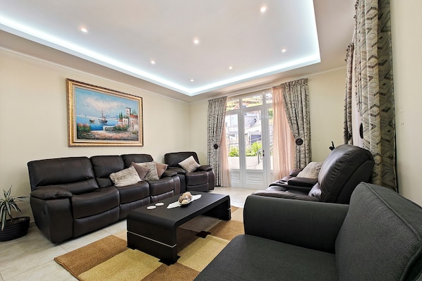 Un salon moderne avec un ensemble de canapés, une table basse, un tableau et une vue dégagée sur l’extérieur grâce à une grande fenêtre.