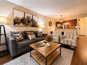 Ein Wohnzimmer mit Sofa, Sesseln, einem Couchtisch, einer Uhr und einem Bild an der Wand.
