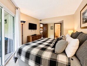 Ein Schlafzimmer mit einem großen Bett, einem Fernseher, einer Kommode und einer Tür zu einem Badezimmer.