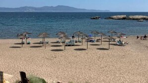 Ein Strand mit Sonnenschirmen und Liegestühlen, ein klarer Himmel und ein ruhiges Meer.