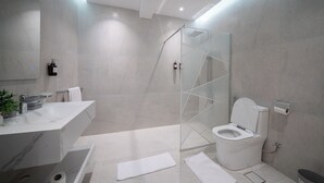A modern bathroom with a glass-enclosed shower, a white toilet, and a vanity with a mirror. - Stylish Rawda Getaway | Comfortable 1BR Apartment (Jeddah)
