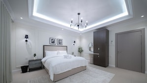A modern bedroom with a large bed, bedside lamps, a chandelier, and a wardrobe. - Stylish Rawda Getaway | Comfortable 1BR Apartment (Jeddah)