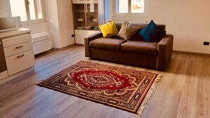Un salon avec un canapé en cuir marron, un tapis à motifs, un meuble blanc et une fenêtre avec des stores.