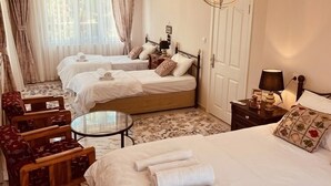 Hotellihuone, jossa on kaksi sänkyä, oleskelualue tuolilla ja pöydällä, kattokruunu ja ovi.