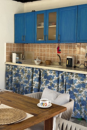 A kitchen with blue cabinets, a tiled backsplash, a wooden table, and a floral curtain.