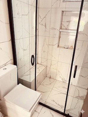 A bathroom with a glass-enclosed shower, a toilet, and a sink.
