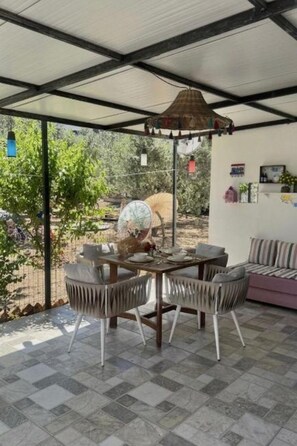A covered patio area with a dining table and chairs, a hanging lamp, and a view of trees and a fence.