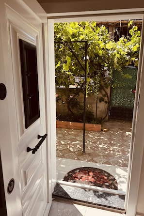 A white door with a black handle, a tiled patio, and a garden with a trellis and greenery.