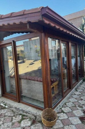 A covered outdoor area with a tiled floor, wooden-framed glass doors, and a woven basket on the ground.