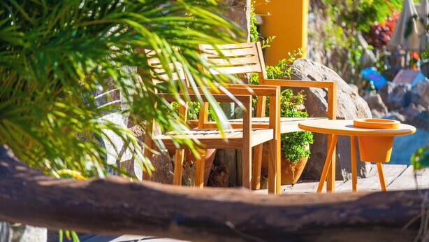 A wooden outdoor seating area with a table and chairs, surrounded by greenery and a rock. - Ifaya Farm (San Miguel)