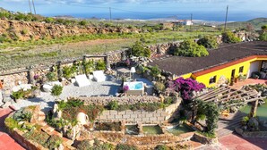 A garden with a pool, a stone wall, and a yellow building. - Ifaya Farm (San Miguel)