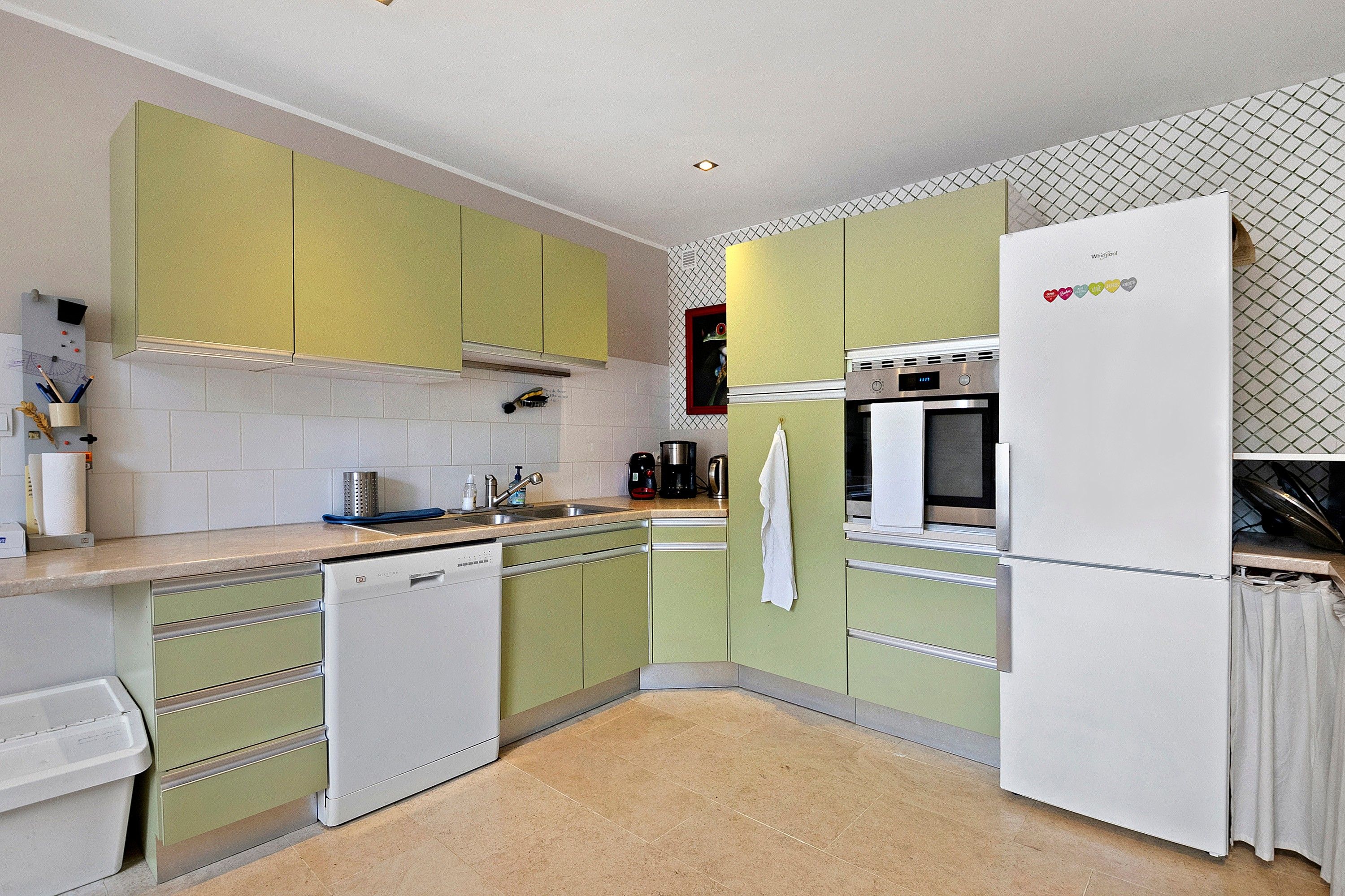 A kitchen with green cabinets, a white refrigerator, and a tiled backsplash.
