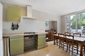 A kitchen with a gas stove, a sink, and a dining area with wooden chairs.