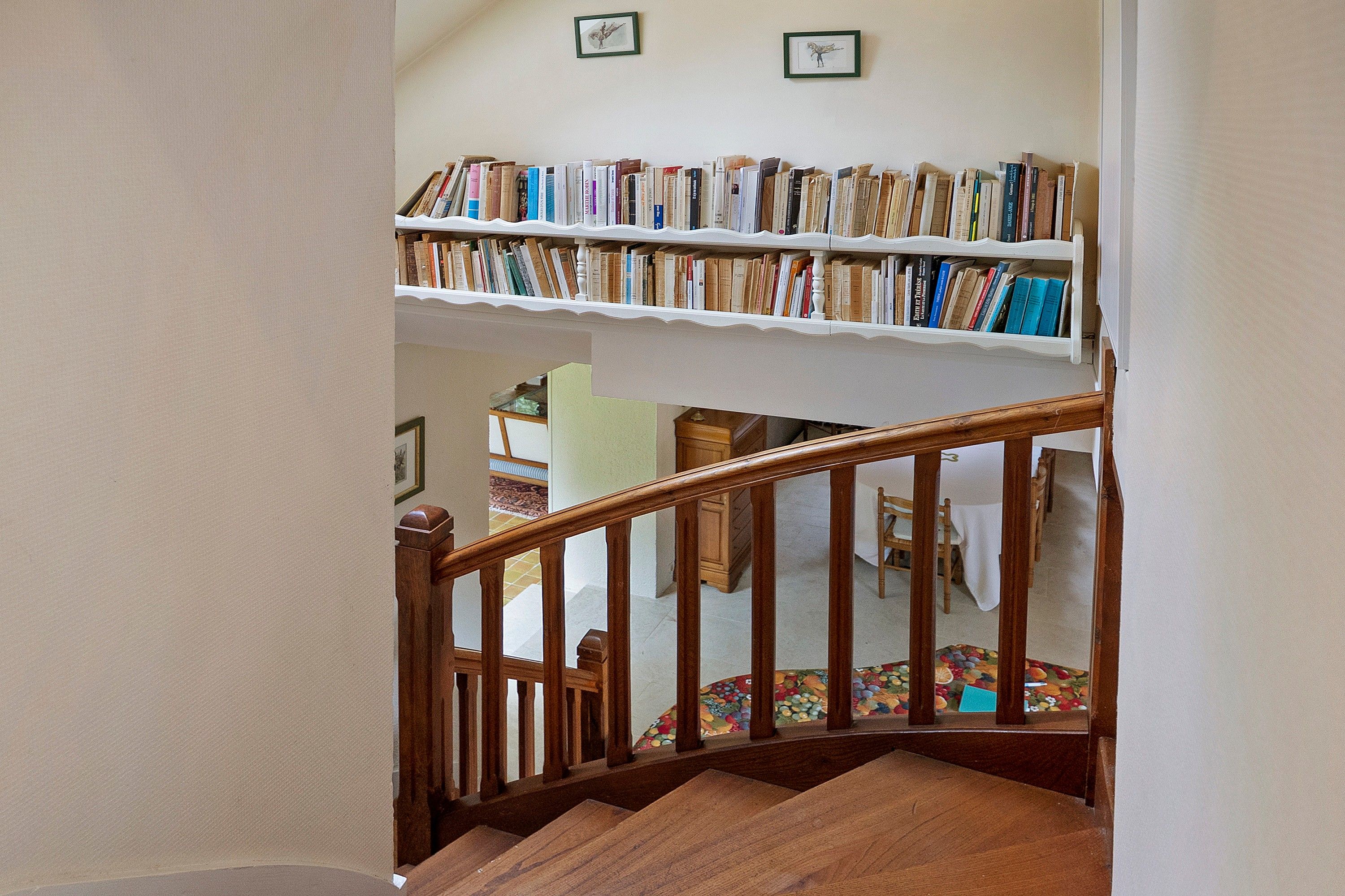 Un escalier avec une rampe en bois menant à un palier où se trouve une bibliothèque remplie de livres.