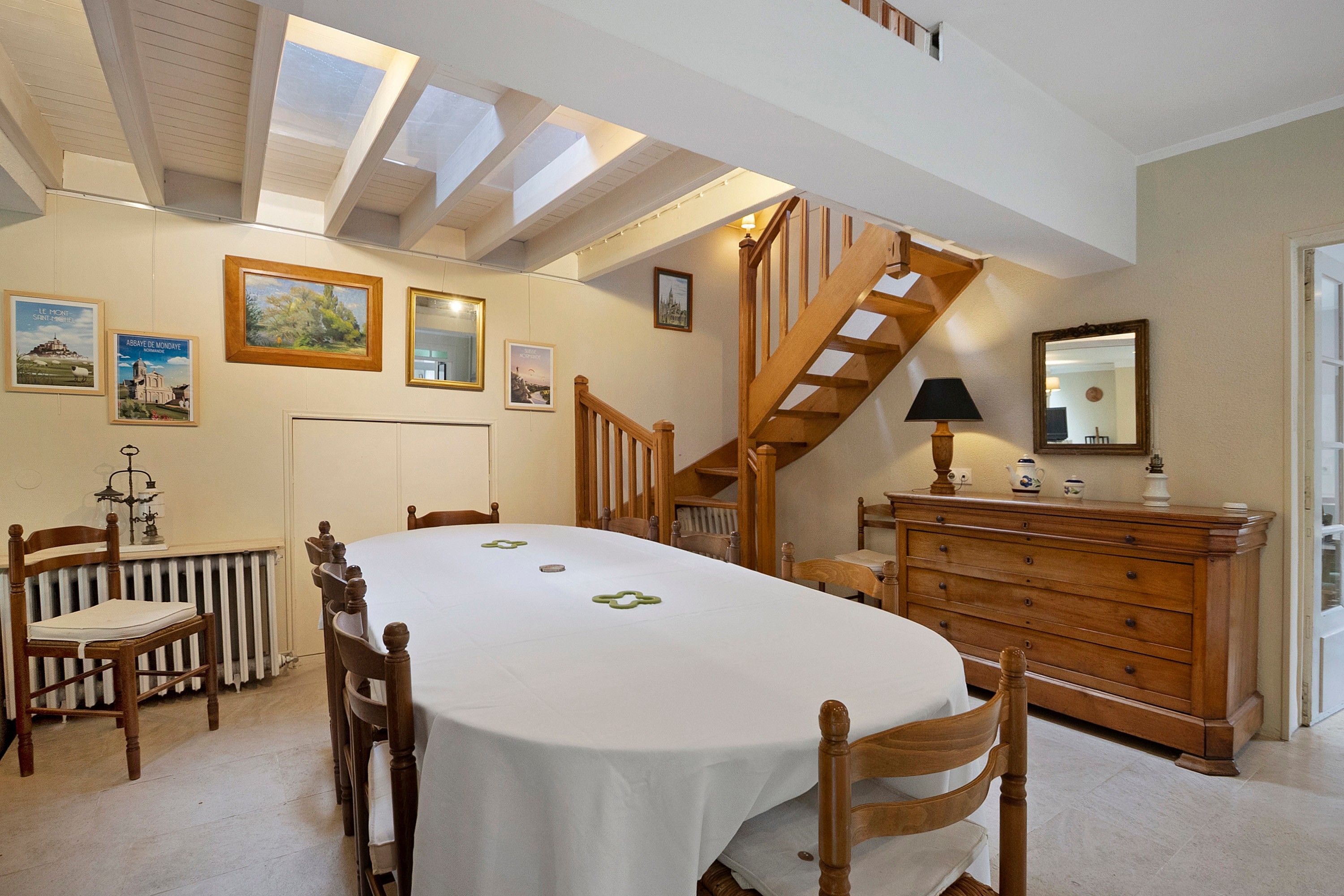 A dining area with a round table, wooden chairs, a staircase, and a dresser with a mirror.