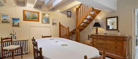 Un comedor con una mesa redonda, sillas de madera, una escalera y un aparador con espejo.
