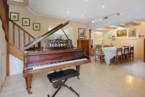 A grand piano in a spacious room with a dining area and a staircase.