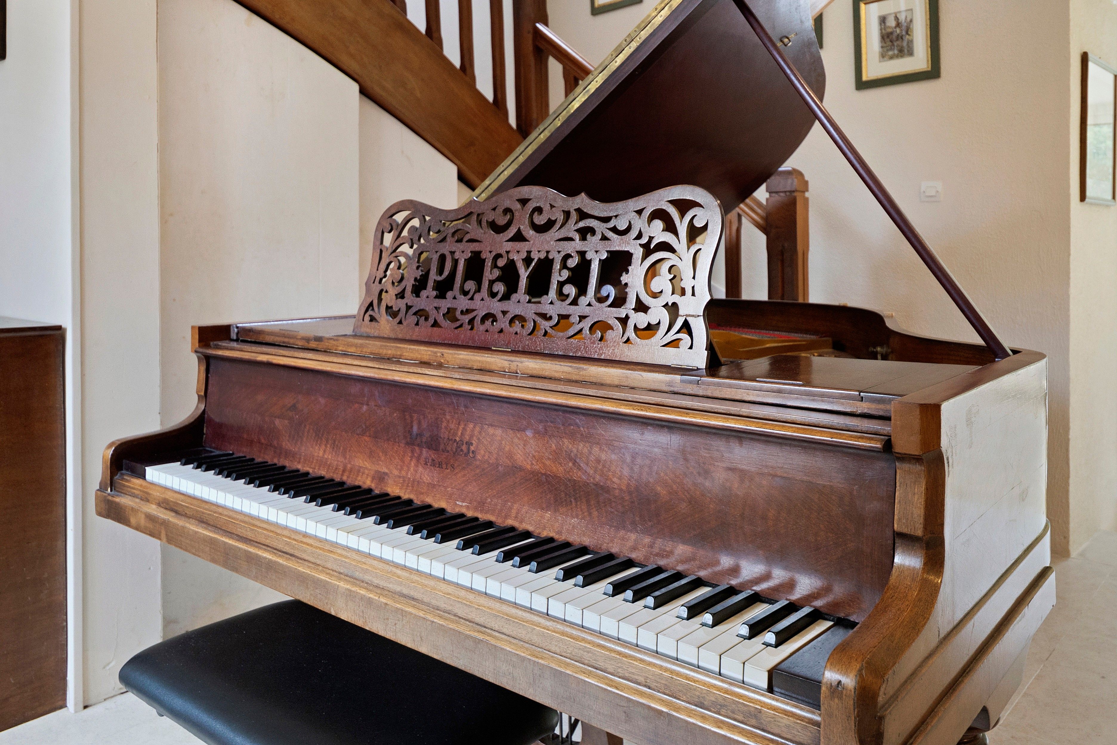 Um piano de cauda com acabamento em madeira e um suporte decorativo em um quarto com escada e quadros na parede.