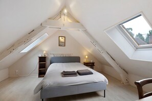 A bedroom with a sloped ceiling, a bed, a nightstand, a lamp, and a window. - Holiday Home 'Le Petit Moulin Du Pré Saint-Gorgon' with Private Terrace, Private Garden and Wi-Fi (Feuguerolles-Bully)
